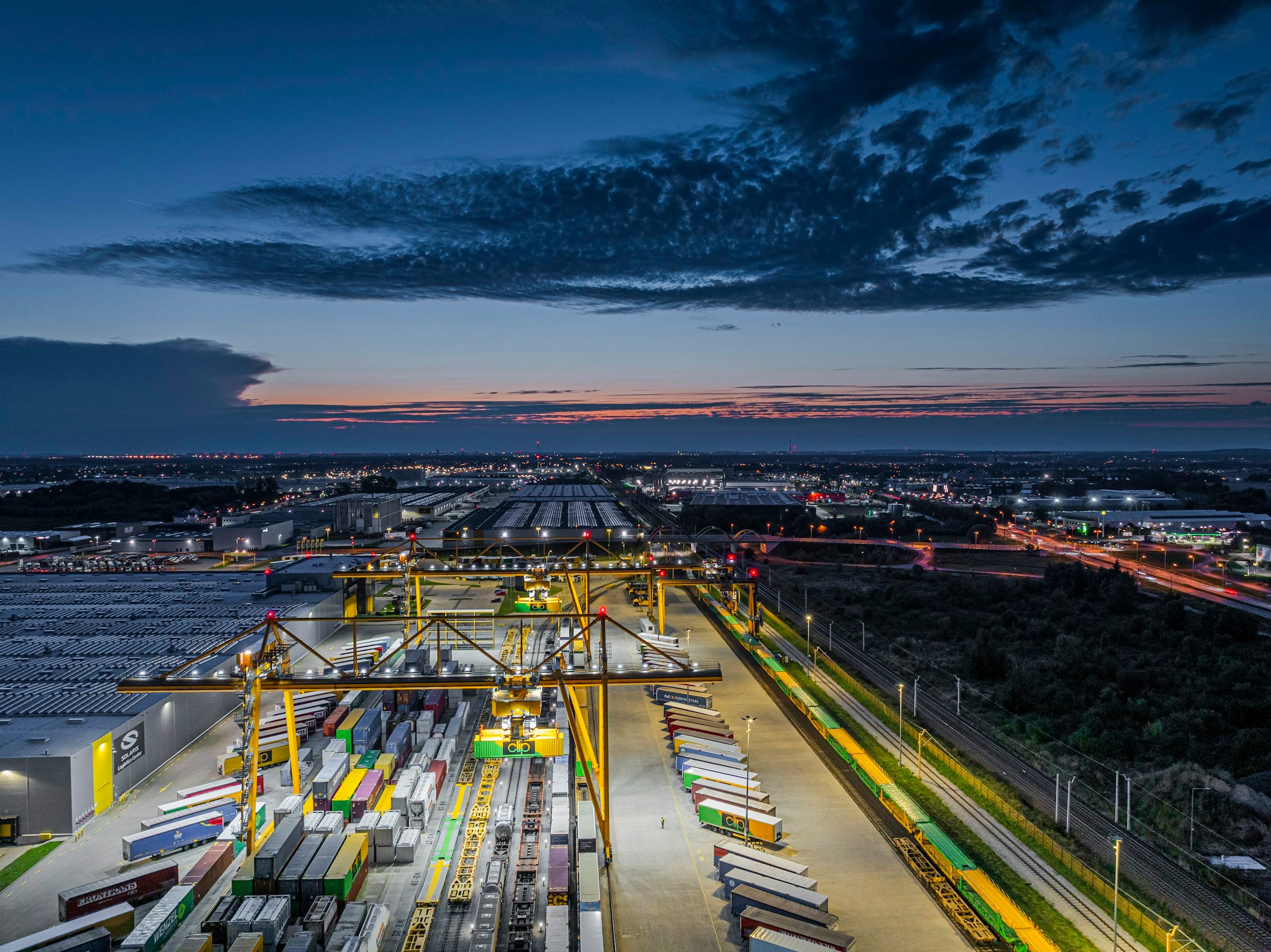 Container terminal with rail-mounted gantry cranes and stacked containers at dusk